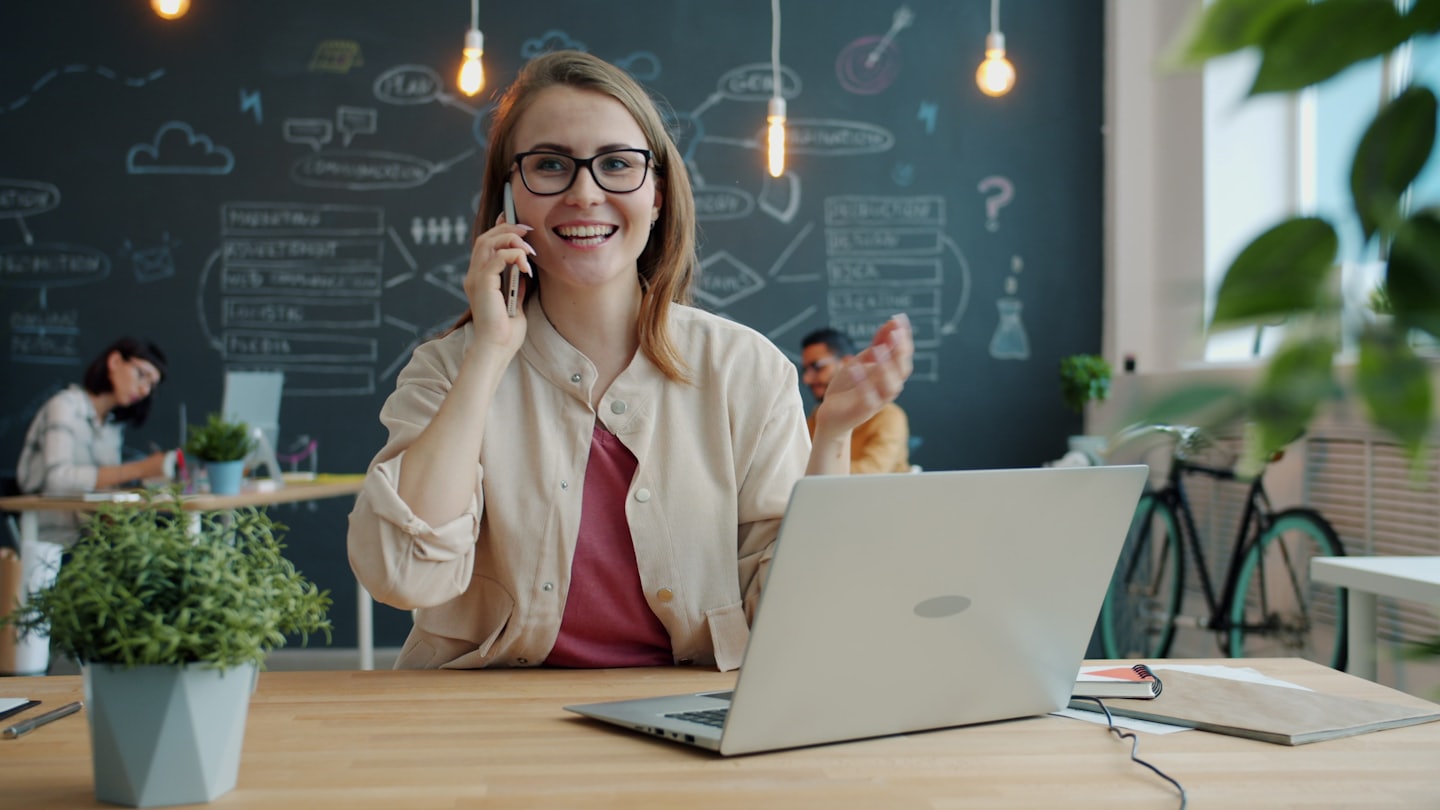 Woman with glasses talks on phone in a modern office.