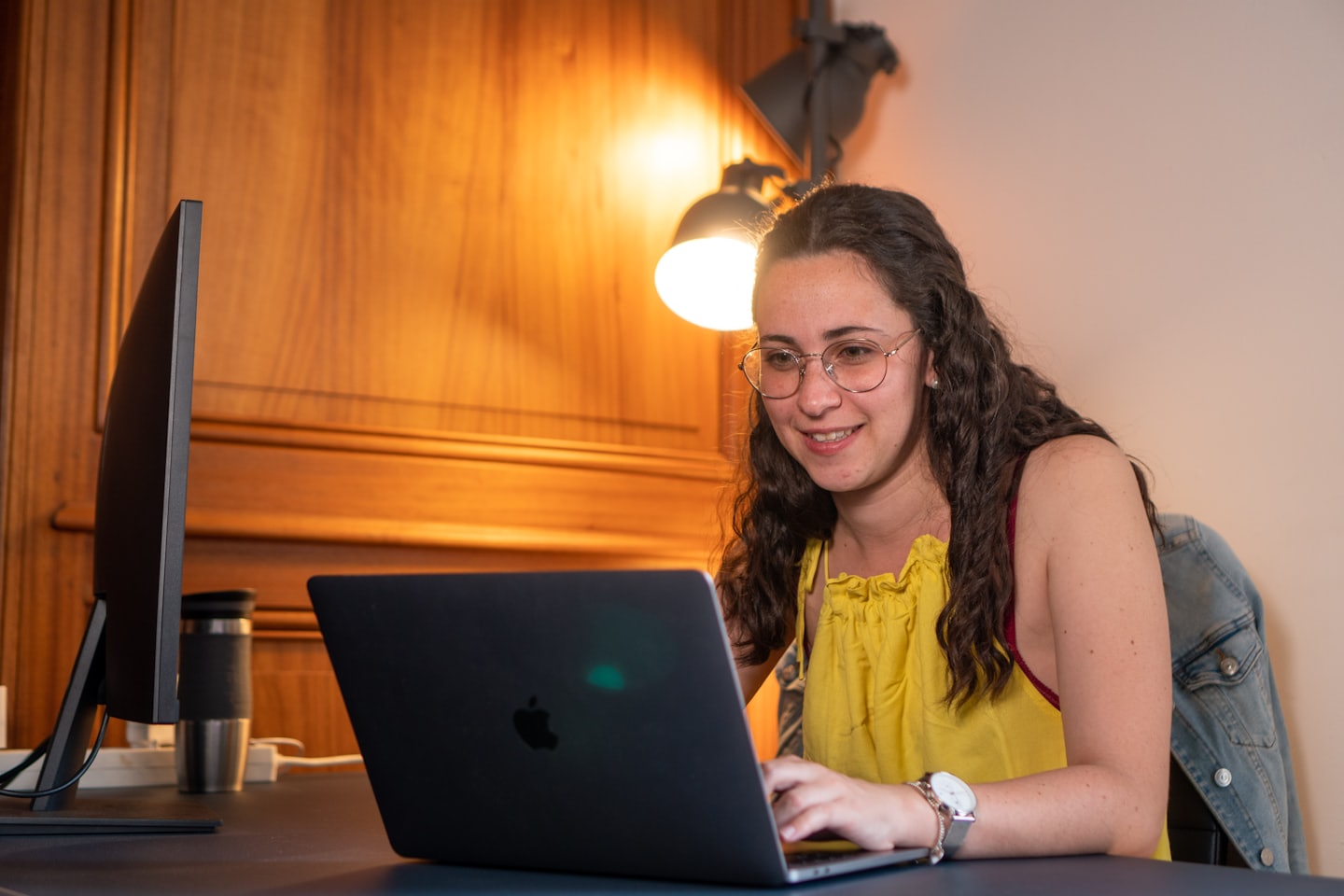 Woman in a yellow top typing on a laptop at a desk.